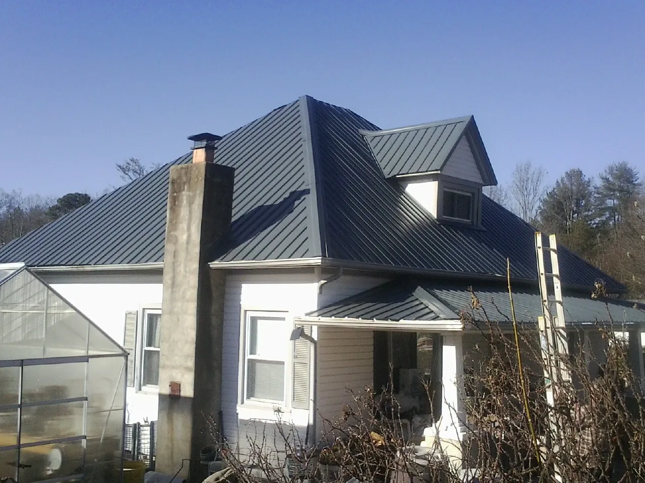 Dark blue standing seam metal roof on a white farmhouse with dormer — Slate & Tile Roof Repair by Roofing Brothers in Ouaquaga