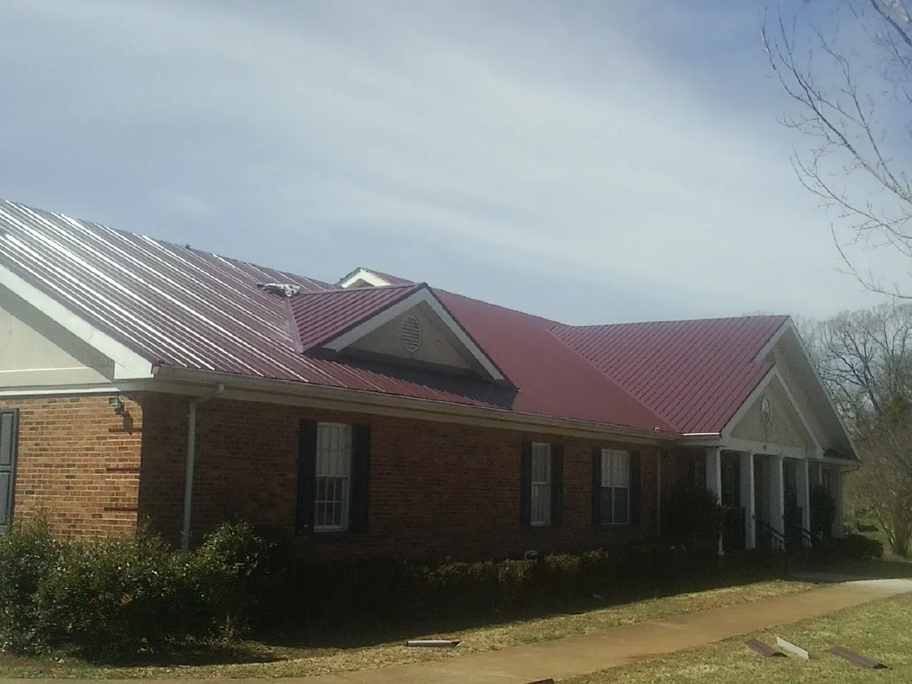 Red metal roof with gabled entries on a long brick building, from a Hail Damage Roof Repair job in Ouaquaga
