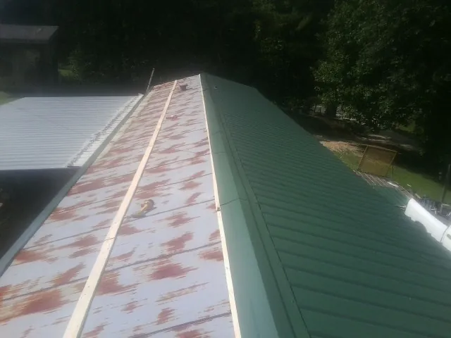 Old rusted panels beside newly installed green metal roofing — Wind Damage Roof Repair by Roofing Brothers in Ouaquaga