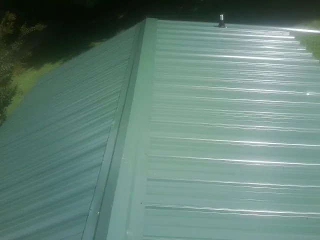 New green metal panels meeting at the ridge of a roof — Flat Roof Repair work by our crew in Ouaquaga