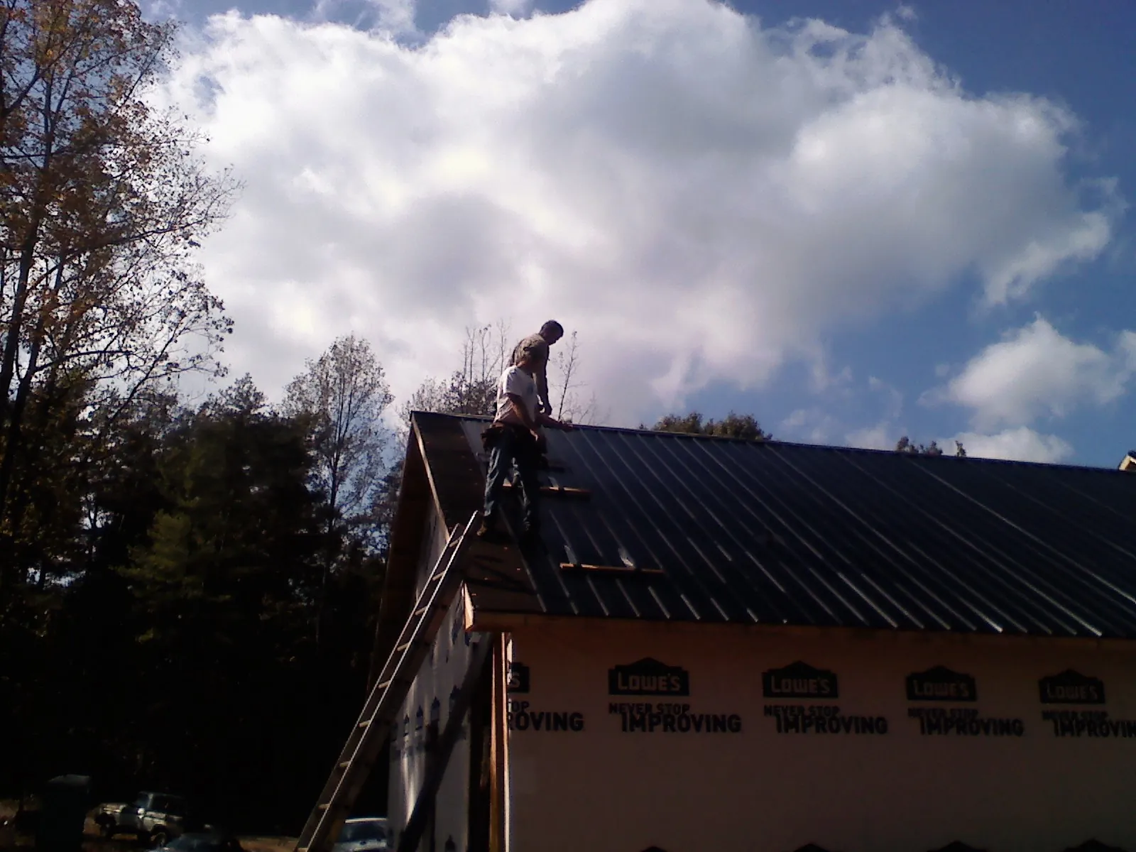 Roofer fastening dark metal panels high against a cloudy sky, from a Roof Inspection job in Ouaquaga