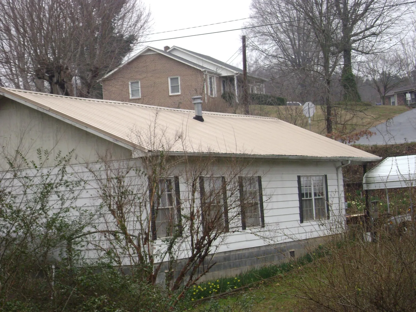 Tan metal roof on a white sided house set into a hillside — Commercial Roofing by Roofing Brothers in Ouaquaga