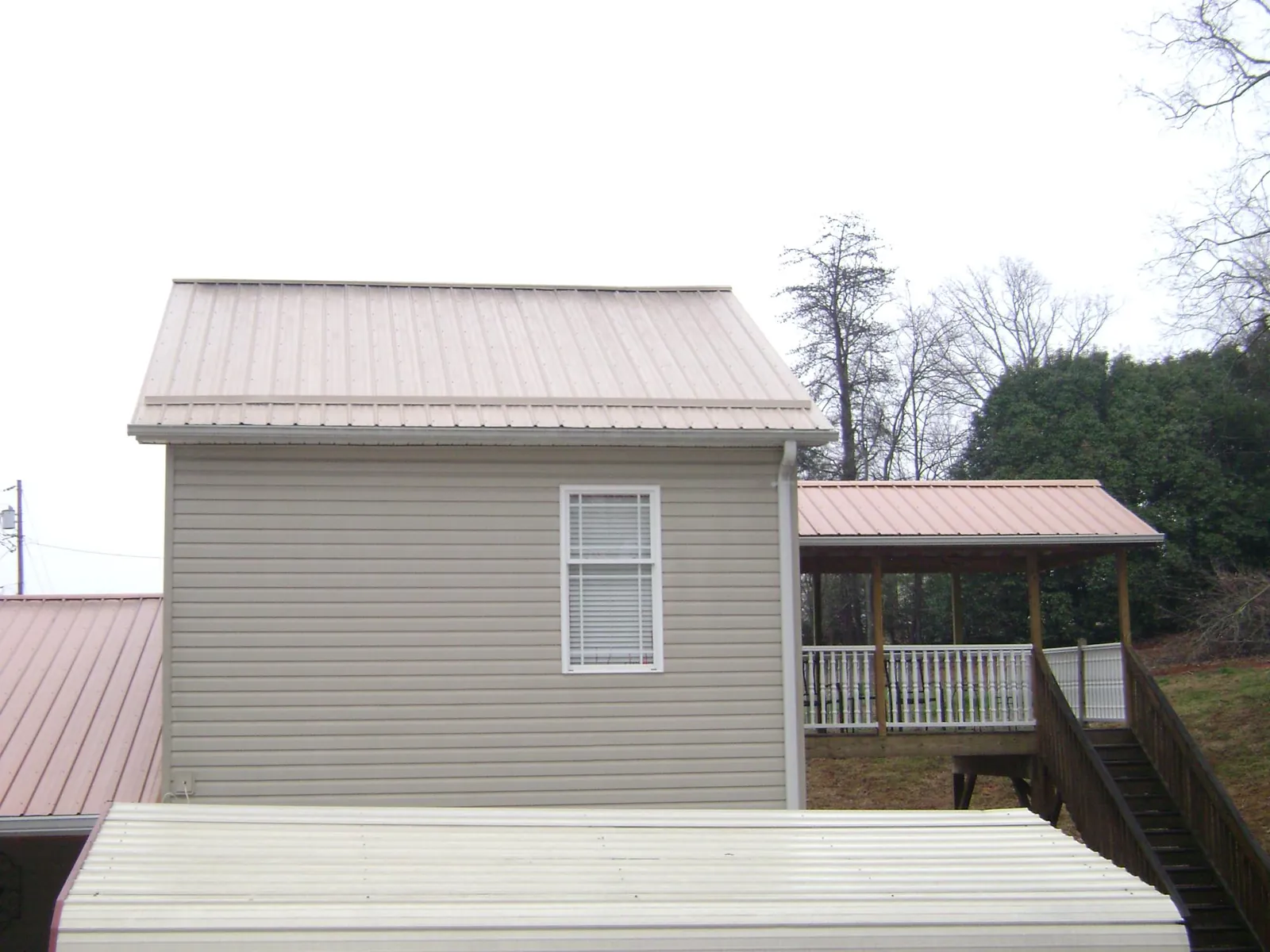 Tan metal roofs on a two story addition and attached porch, from a Roof Replacement job in Ouaquaga